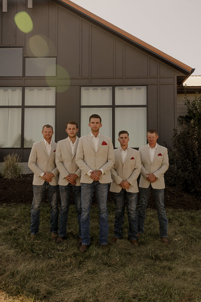 groomsmen poses standing in front of barn in iowa