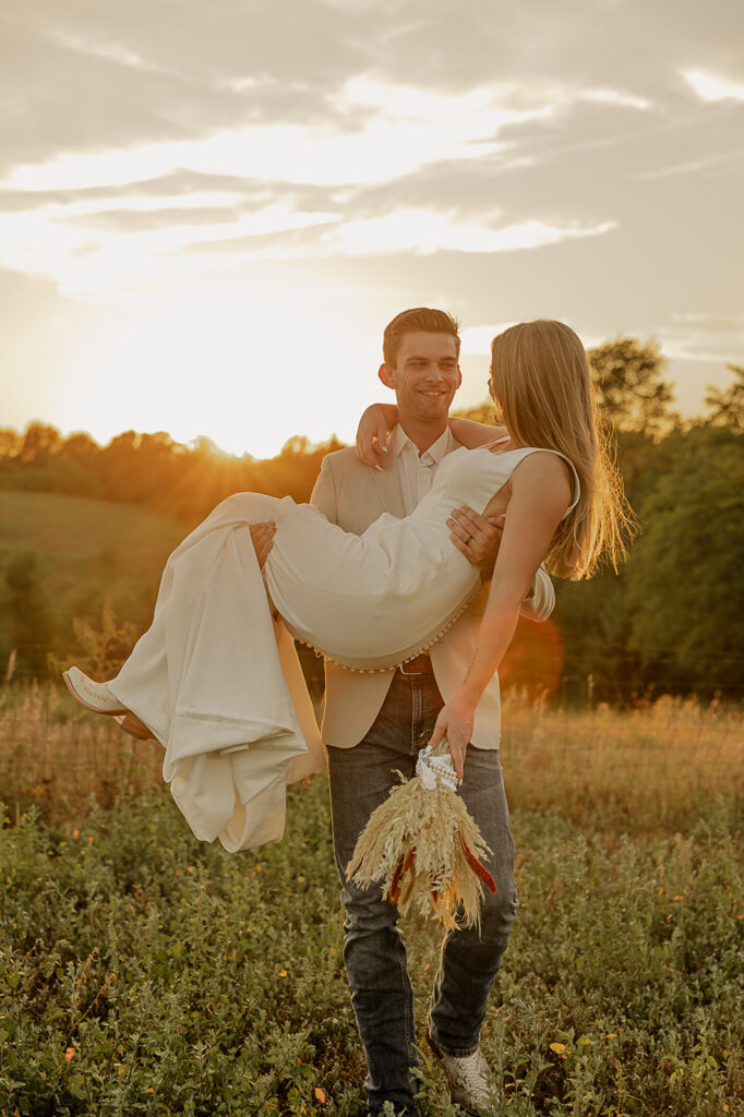 groom lifting bride in field during golden hour