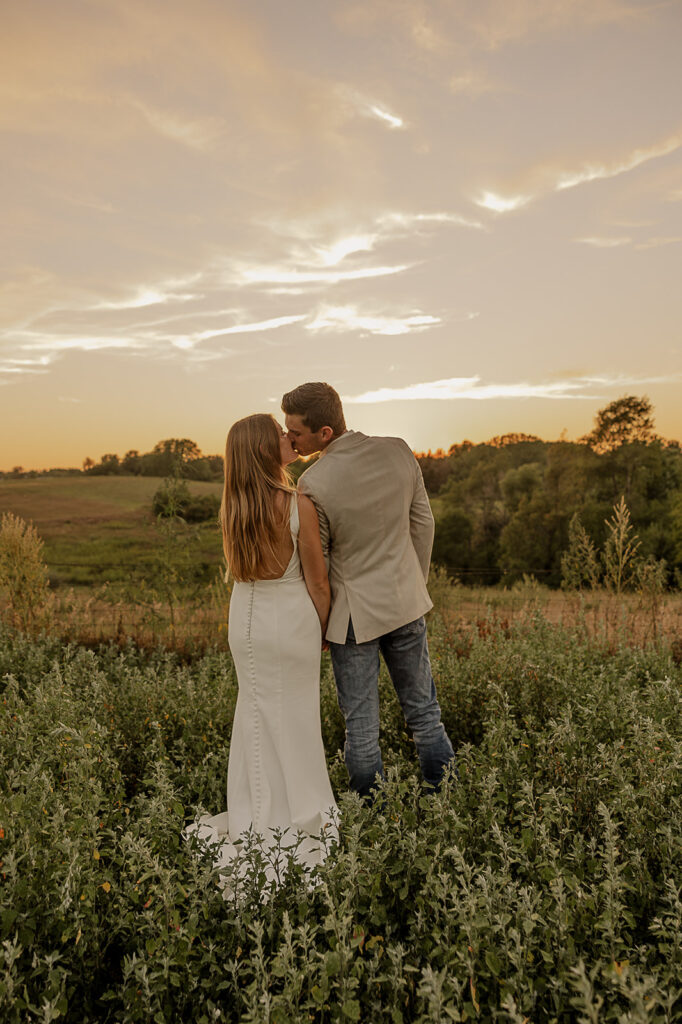 bride and groom standing in a field during sunset portraits iowa wedding photographer