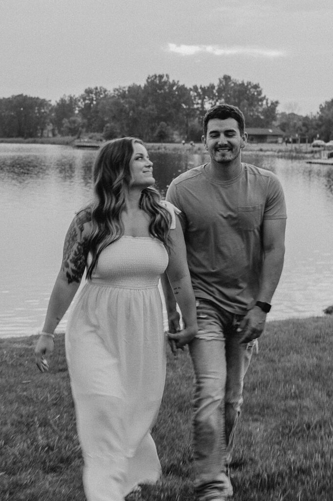 couple holding hands and walking with pond in the background