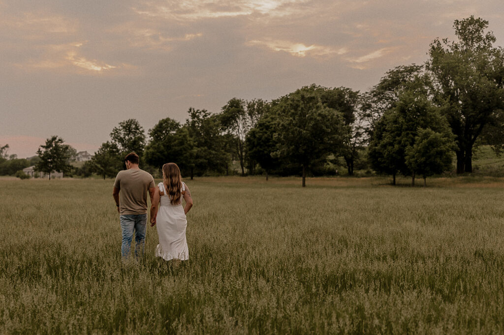 couple holding hands and walking in field during golden hour