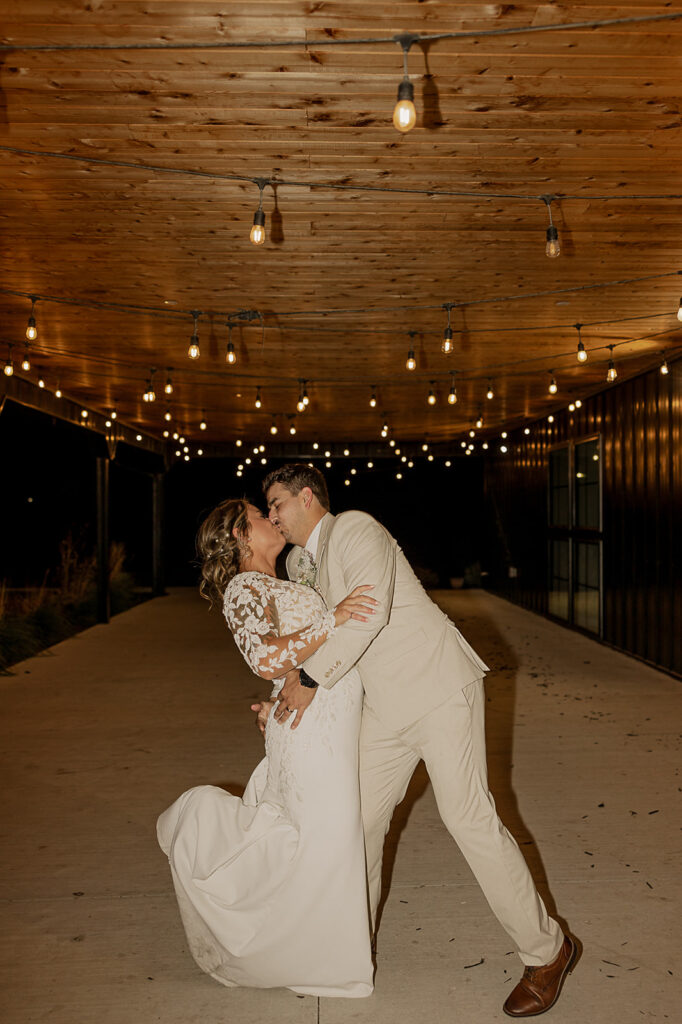 bride and groom dip kiss pose underneath cafe lights wedding exit