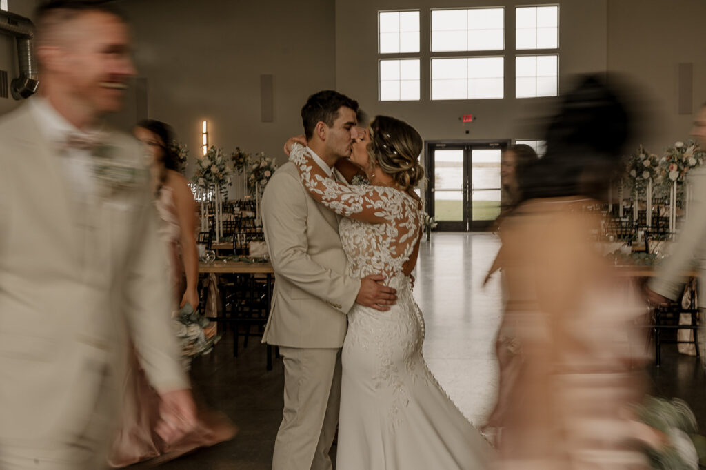 blurry bridal party photos with still bride and groom kissing in the middle