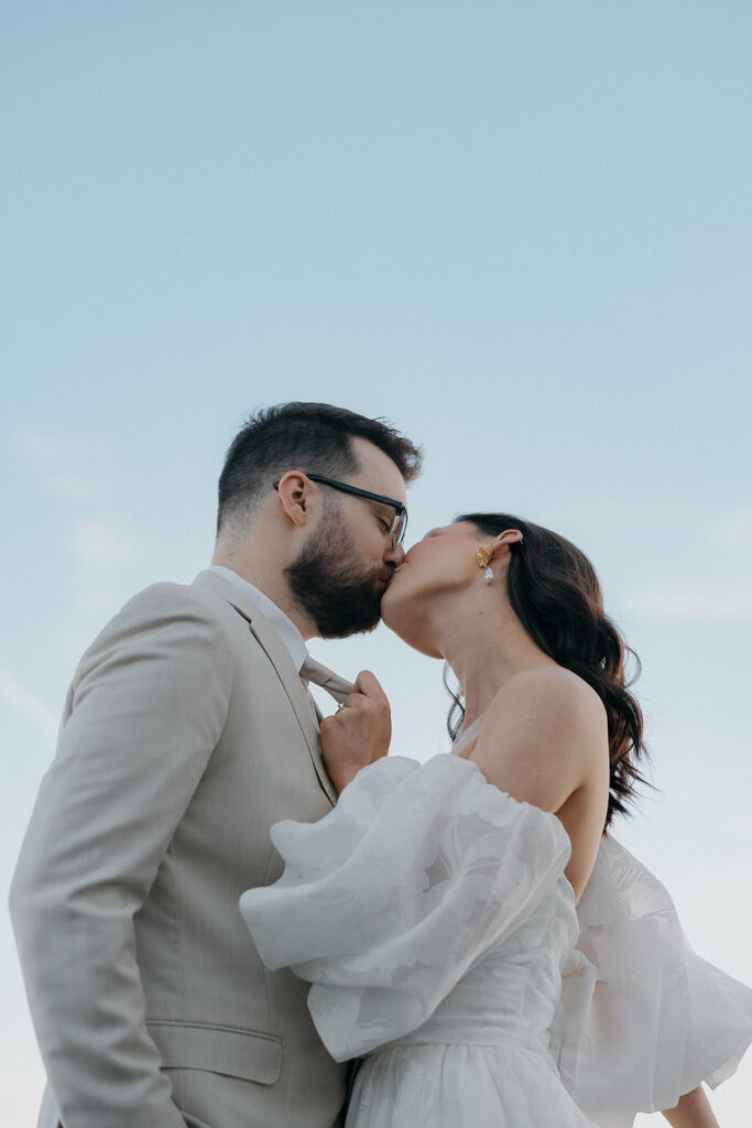 bride kissing groom and holding his tie