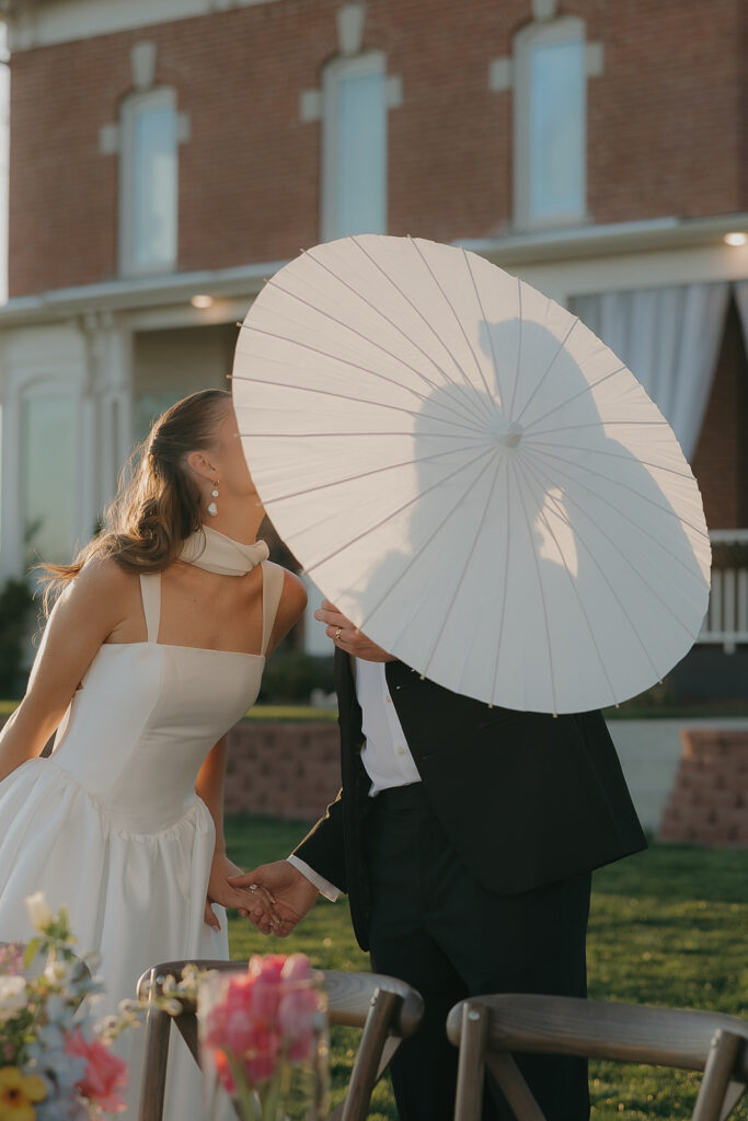 bride and groom kissing behind umbrella questions to ask your wedding photographer