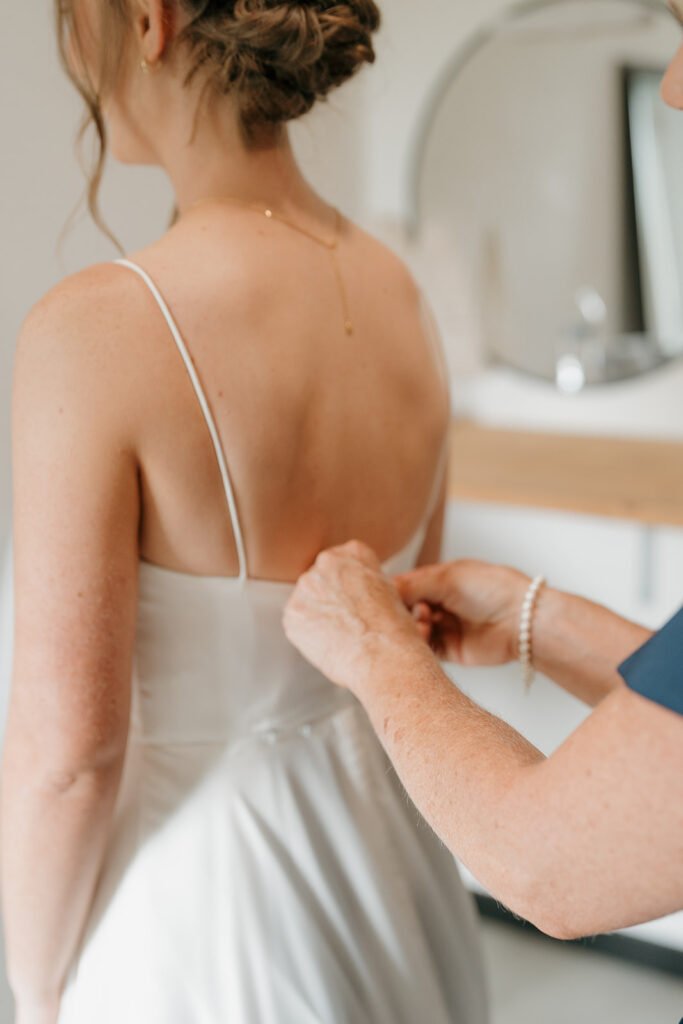 Detail photo of the brides mom buttoning up her dress as they get ready