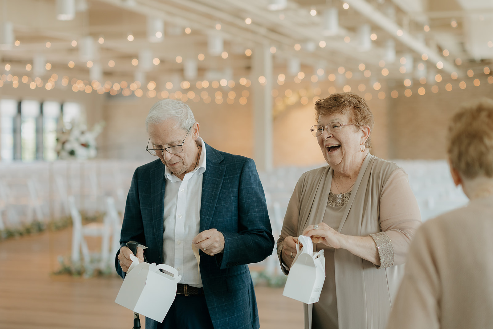 Guests opening small white favor boxes and laughing together before the reception