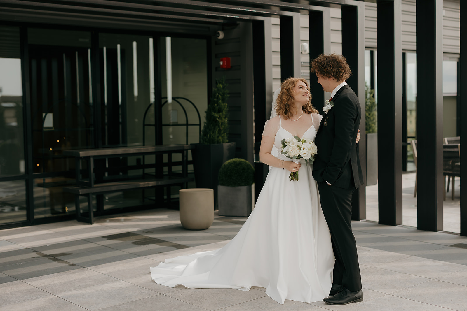 Bride and groom standing together outside the venue, looking at each other while holding a bouquet