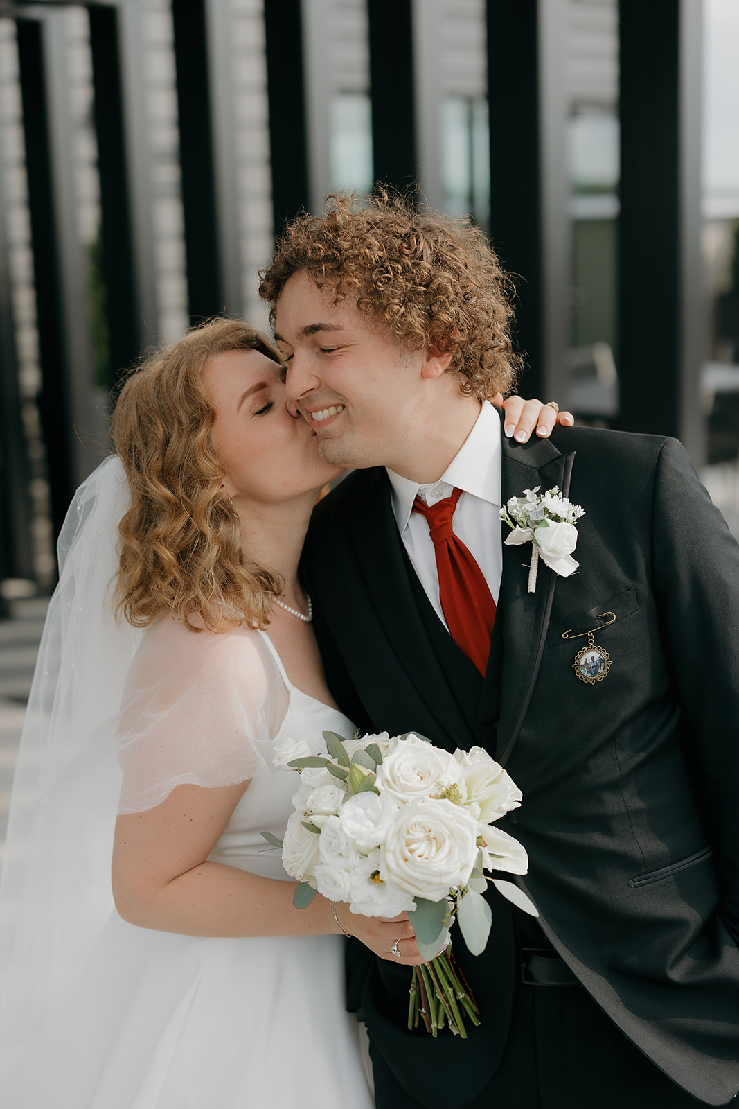 Bride kissing the groom’s cheek while holding her white rose bouquet, a candid moment that reflects documentary wedding photography