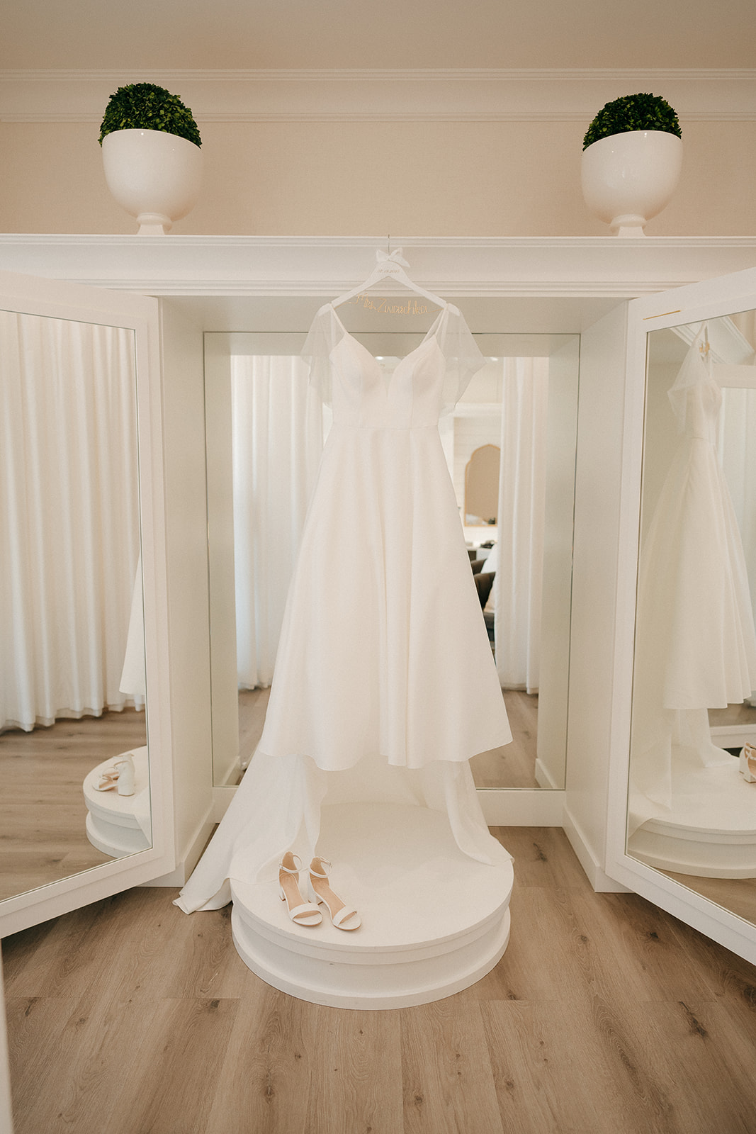 Wedding dress hanging in a bright bridal suite with mirrors and natural light, showcasing the simple and elegant gown through documentary wedding photography