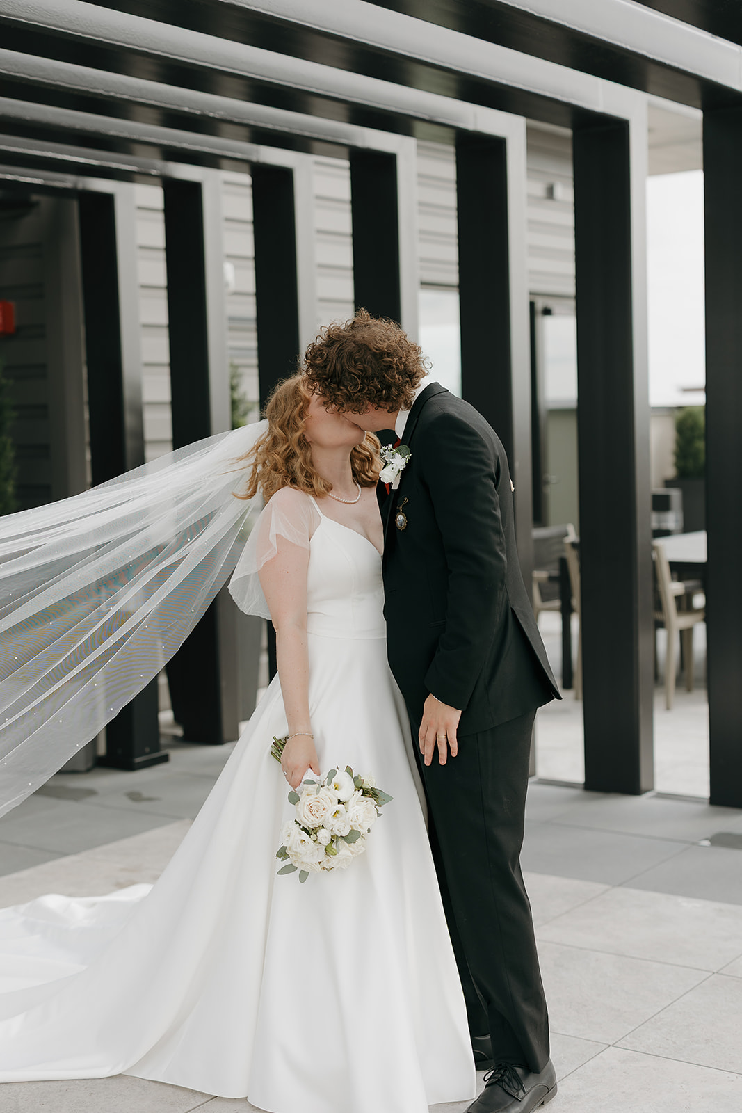 Bride and groom kissing outside their venue during their bride and groom portraits with the brides veil flowing behind her.