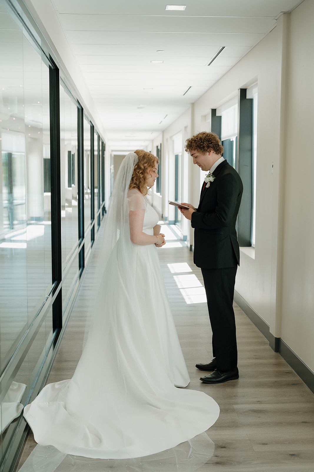 Bride and groom exchanging vows in the hallway, facing each other with natural light streaming in