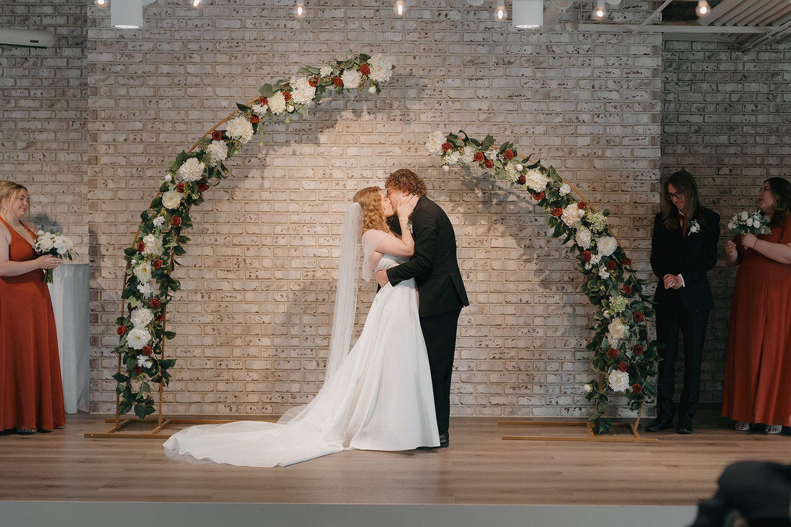 Bride and groom sharing their first kiss at the altar beneath floral arches