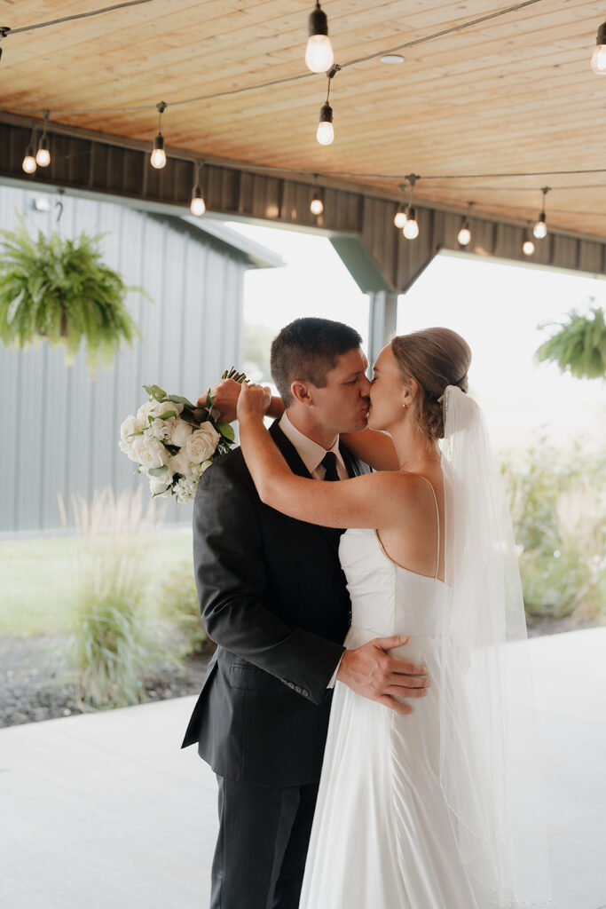 The bride and groom kissing under string lights.
