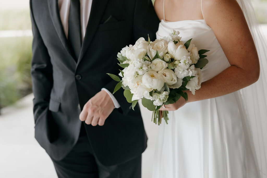 A detail photo of the bride and groom walking together, the photo is focusing the brides florals and dress as well as the grooms suit.