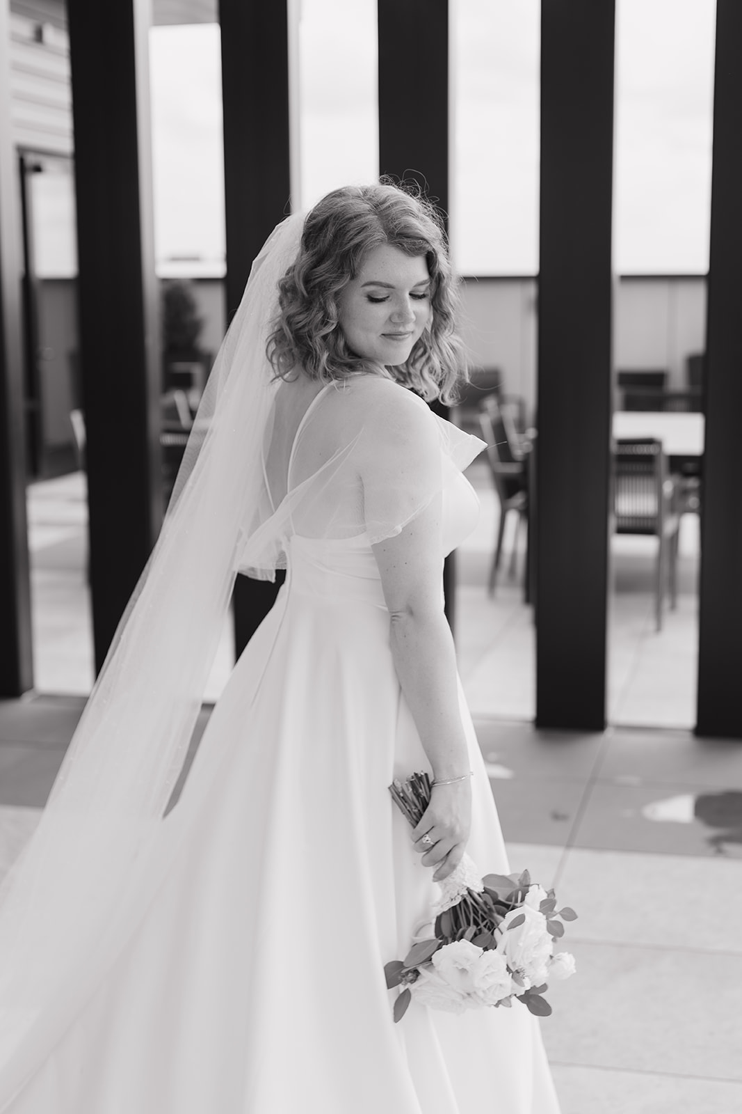 Black and white photo of the bride looking back over her shoulder towards her dress to show casecase her beautiful wedding dress
