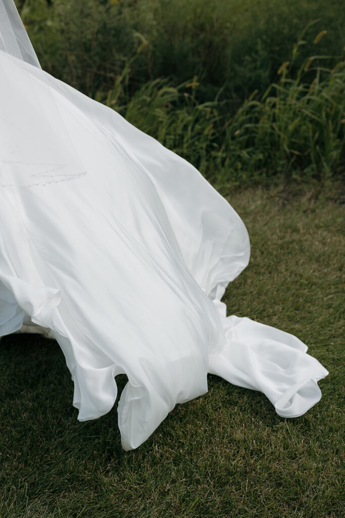Detail shot of brides dress flowing on the grass during at their outdoor wedding venue in Iowa