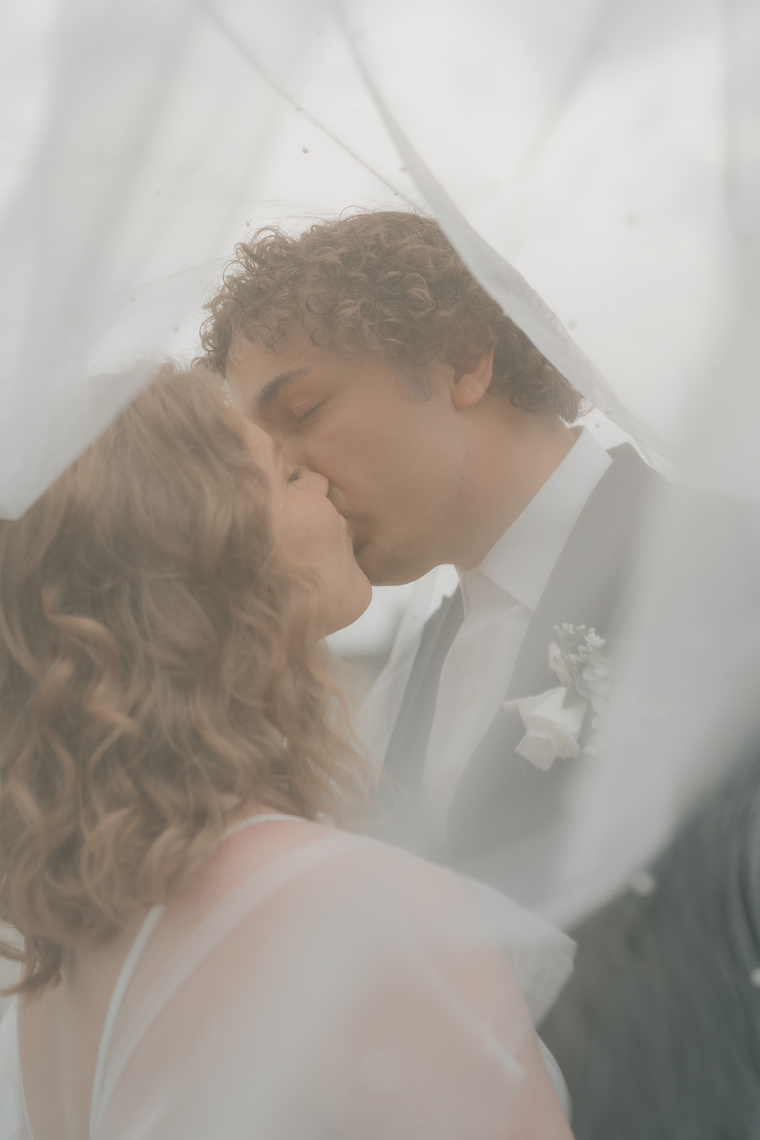 Bride and groom sharing a soft kiss under the veil, a dreamy moment captured through documentary wedding photography
