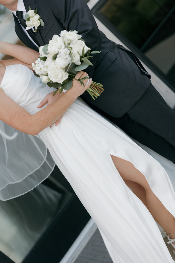 Detail photo of the bride and groom hugging to showcase the grooms suit, the brides dress, and the white florals