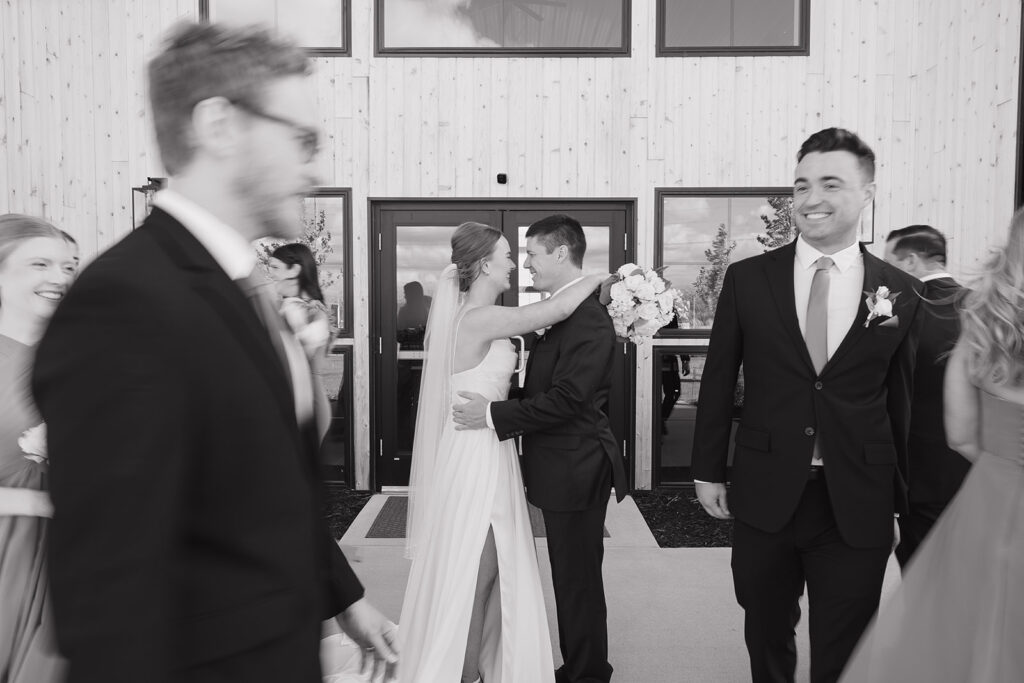 A blurry shot of the bride and groom standing in front of their outdoor wedding venue as the wedding party walks around them