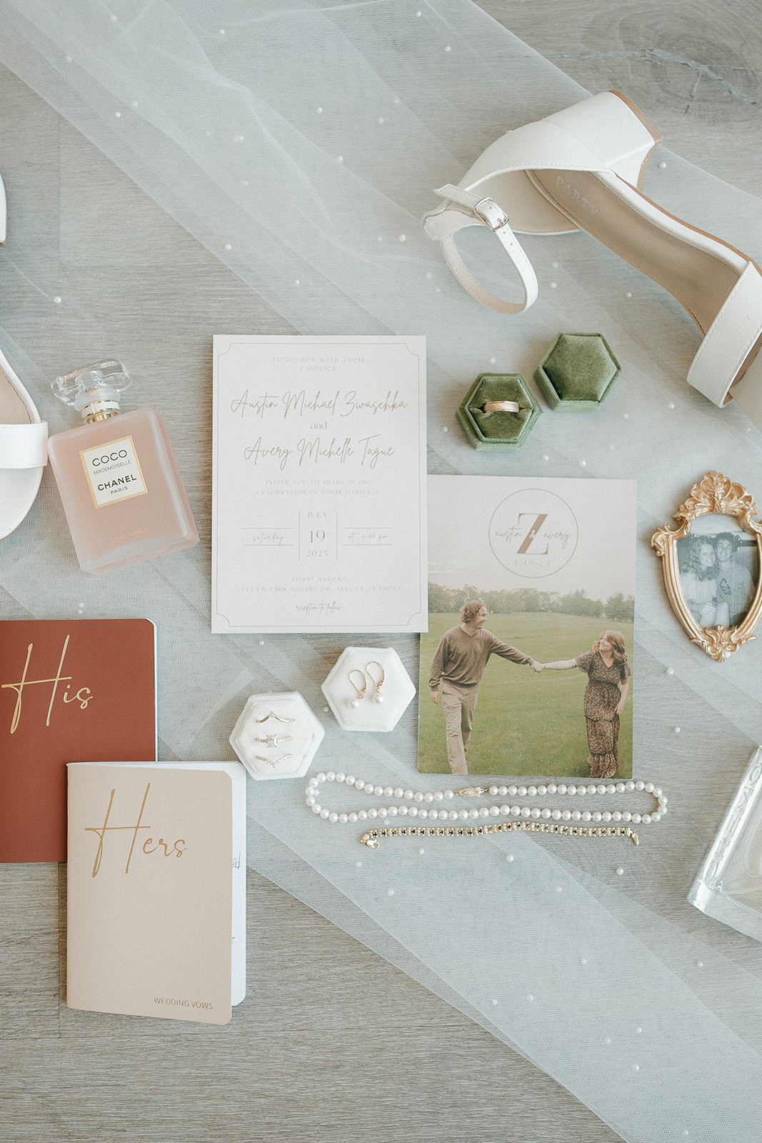 Flatlay of wedding details including rings, vow books, lace, and white bridal shoes arranged on the floor alond with their wedding invites and photos.