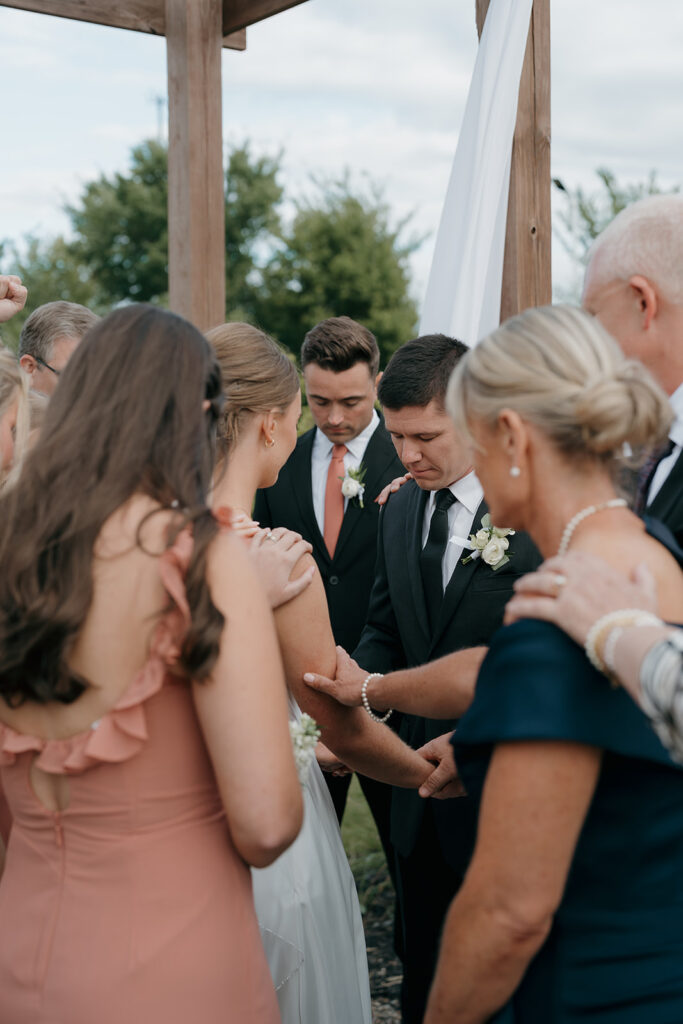 The wedding guests huddled around the bride and groom to pray over them during the ceremony at their outdoor wedding in Iowa