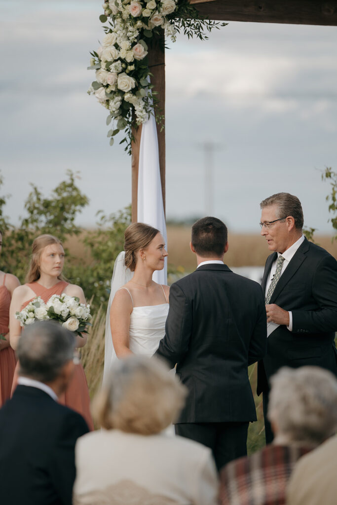A photo of the bride and groom smiling at the officiant during their ceremony.