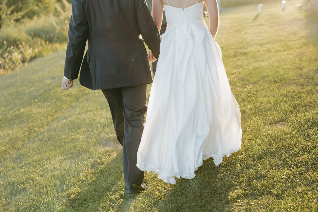 Documentary style photo of the bride and groom walking towards the sunset, detail shot from the shoulders down.