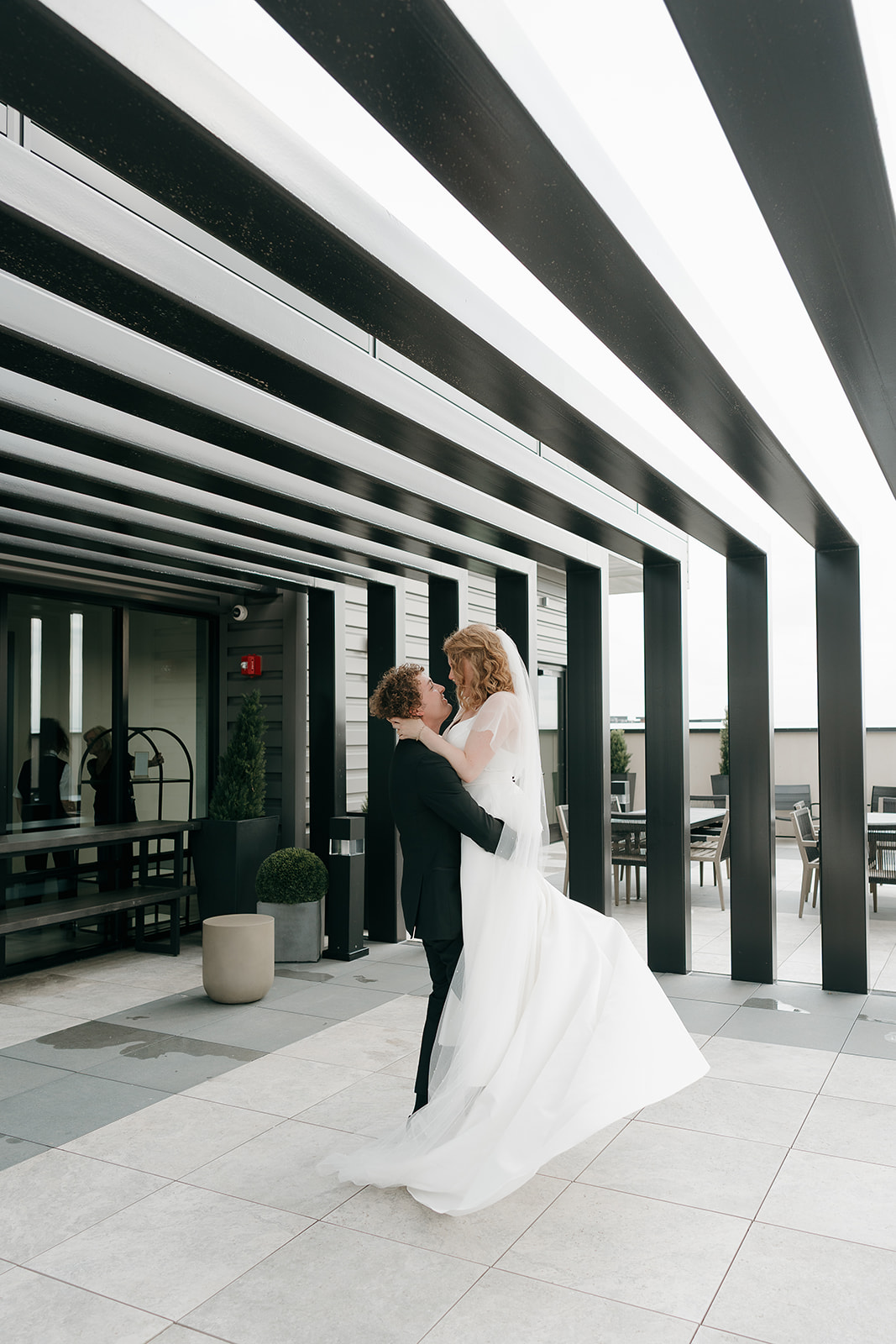 Groom lifting the bride slightly as they laugh together outside the venue