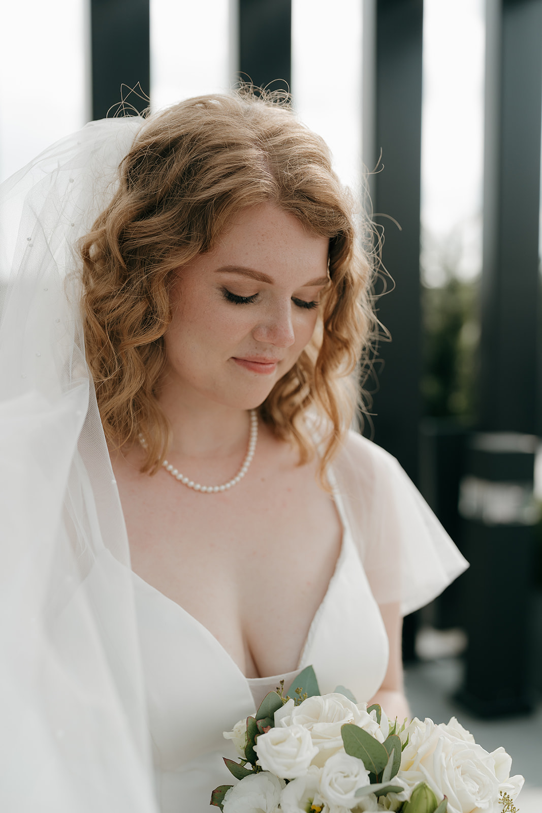 Bride holding her bouquet, looking down softly with her veil draped over her shoulder