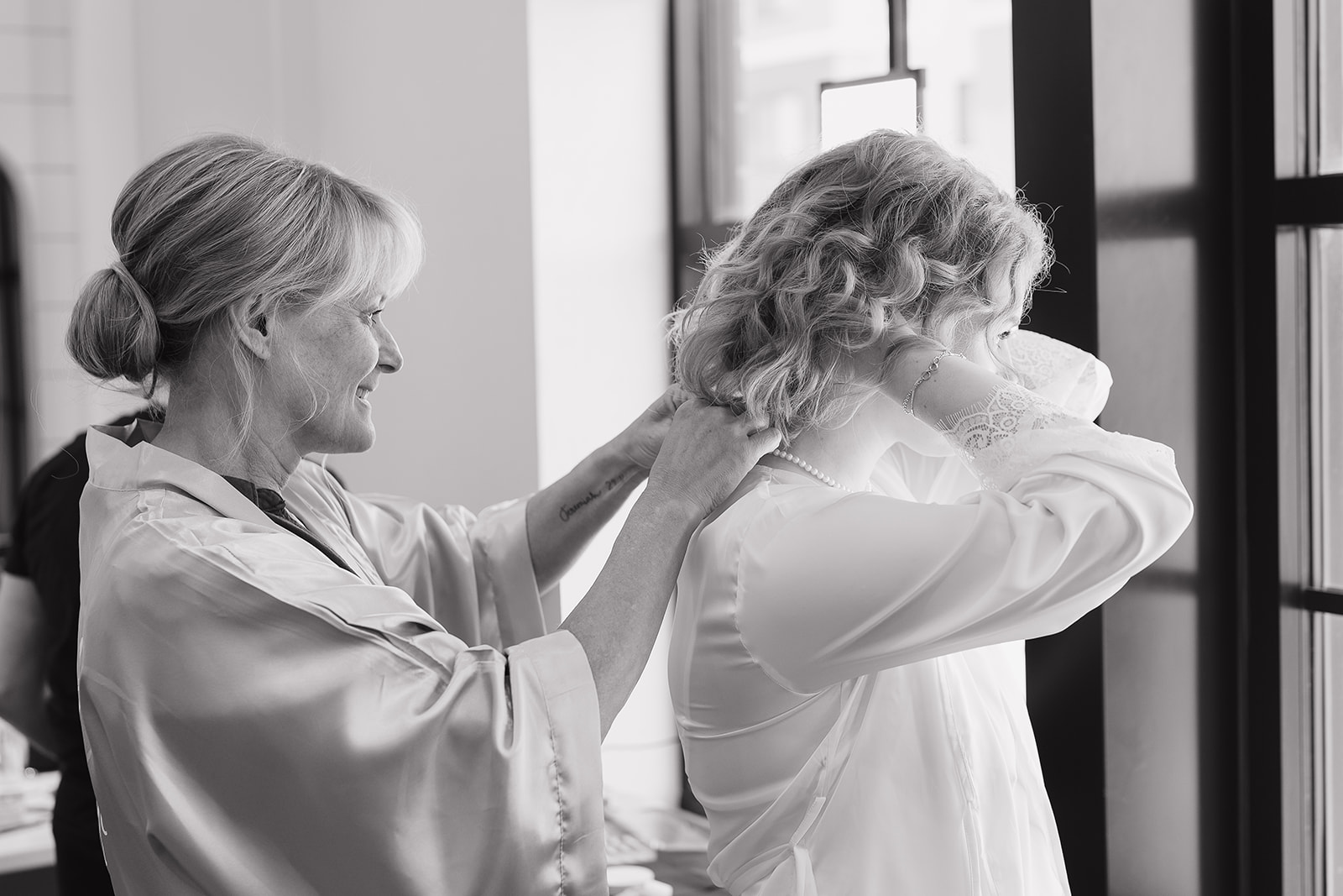The bride's mom clasping a necklace around the brides neck.