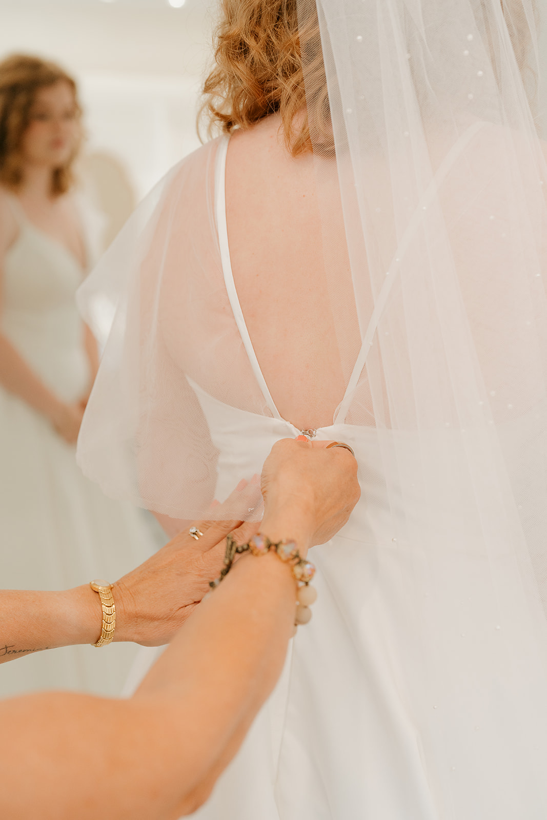 The bride's mom helping the bride with her dress by zipping it up. Captured by a Des Moines Wedding Photographer.