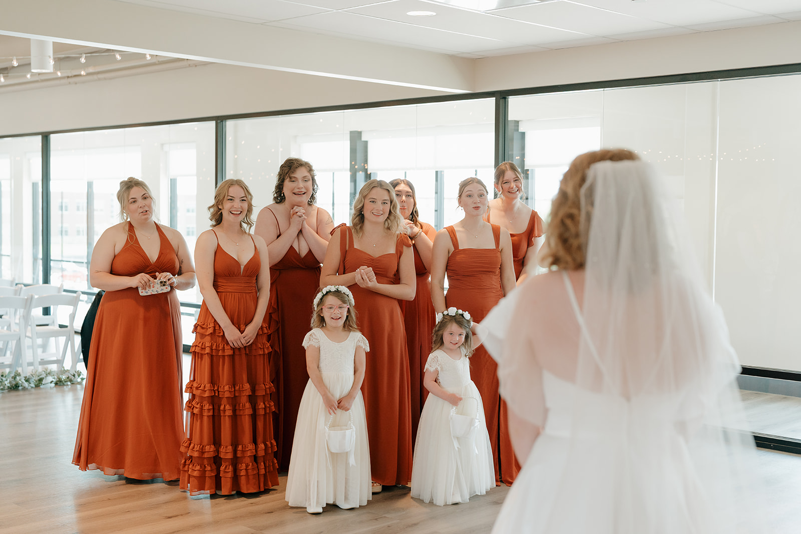 A reaction photo of the bridesmaids and flower girls seeing the bride in her dress for the first time. Captured by a Des Moines Wedding Photographer.