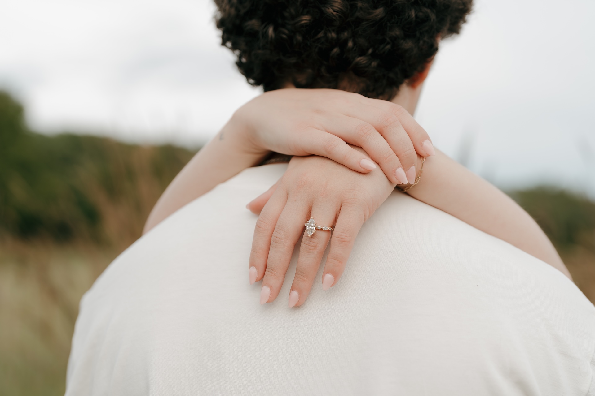 Close-up detail of an engagement ring resting on a partner’s shoulder, photographed outdoors at one of their chosen Engagement Photo Locations.