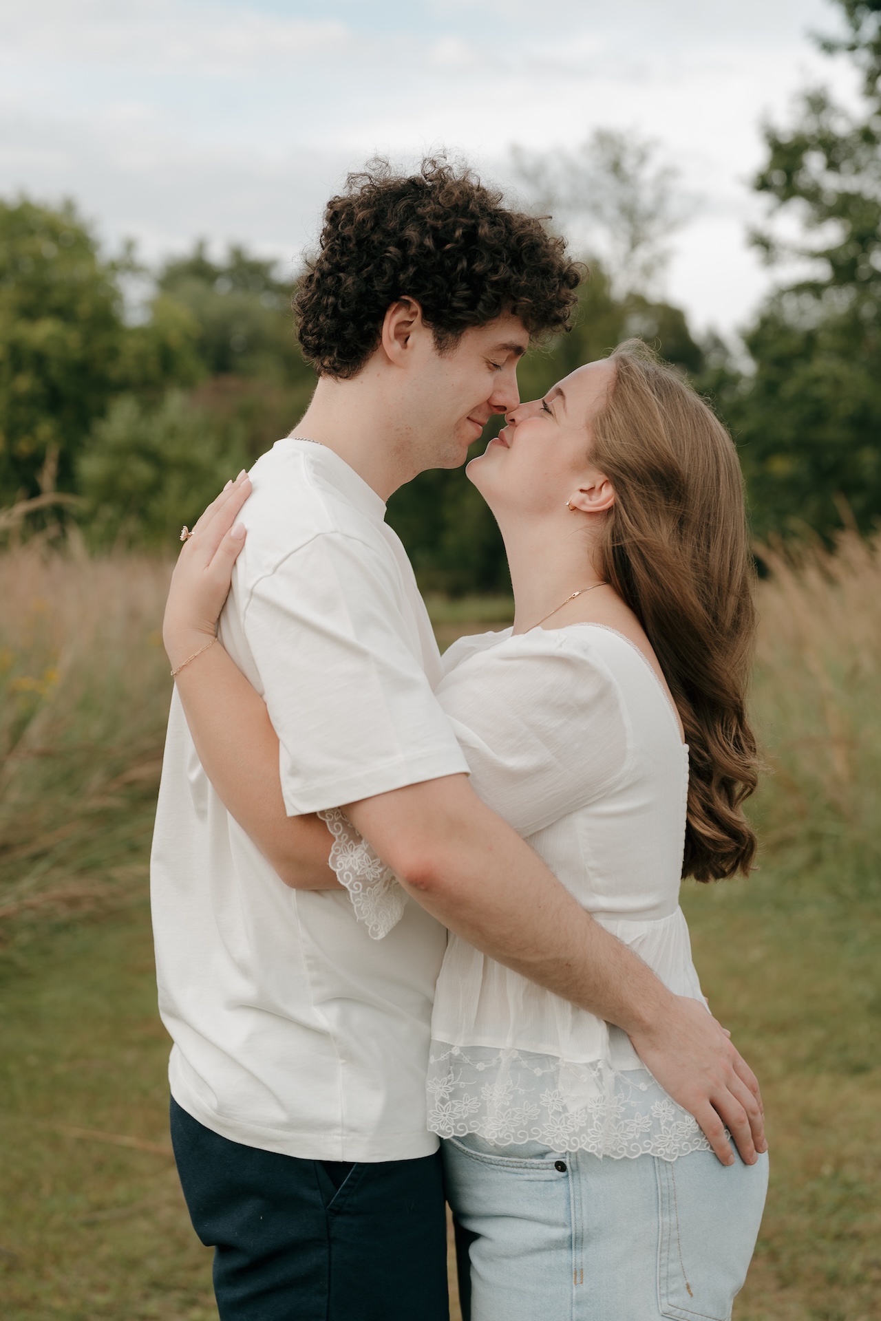 Couple standing nose to nose in a grassy field, arms wrapped around each other during an outdoor engagement session.