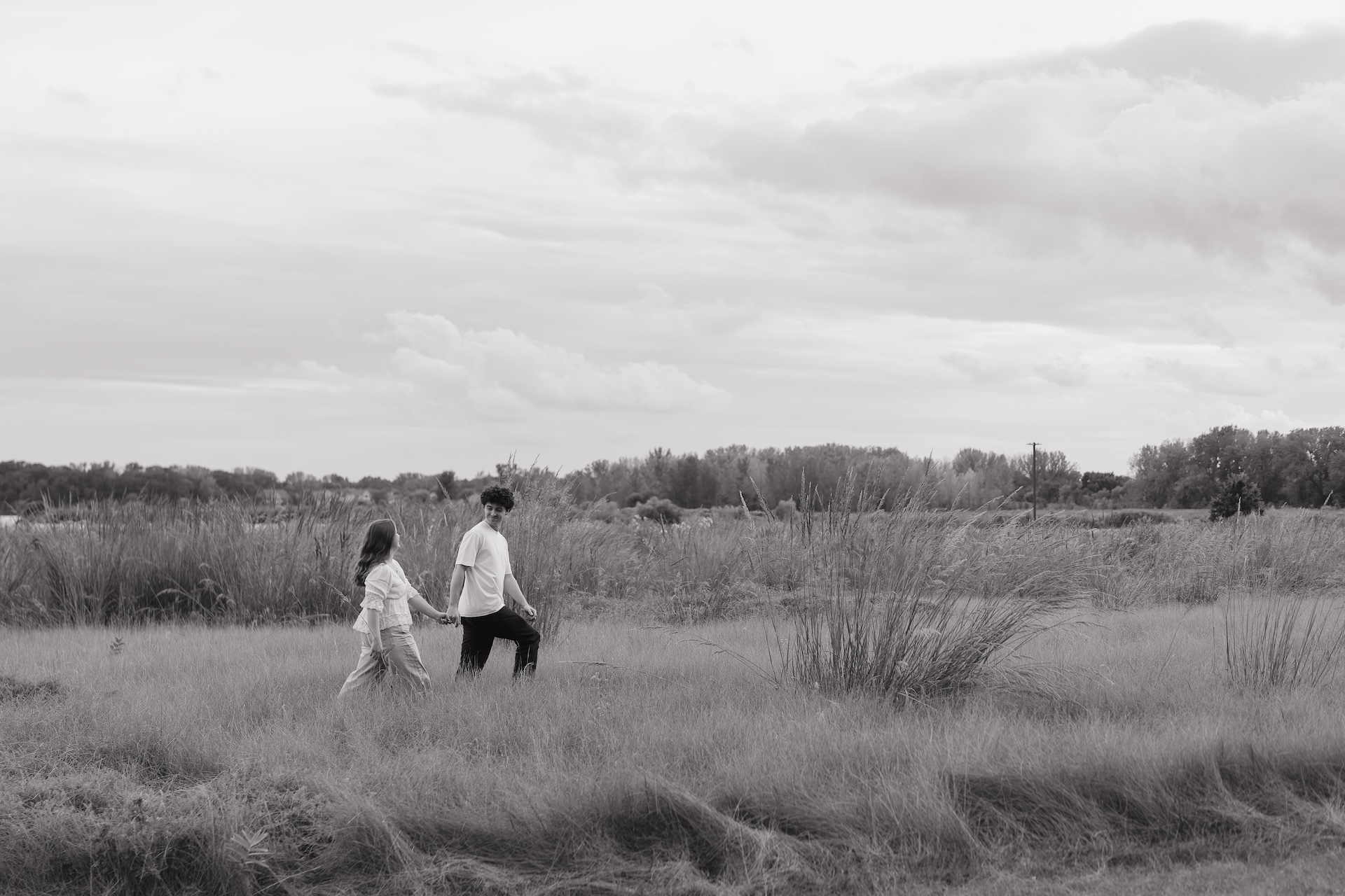 Black and white engagement photo of a couple holding hands while walking through an open field, creating a candid and documentary-style moment.