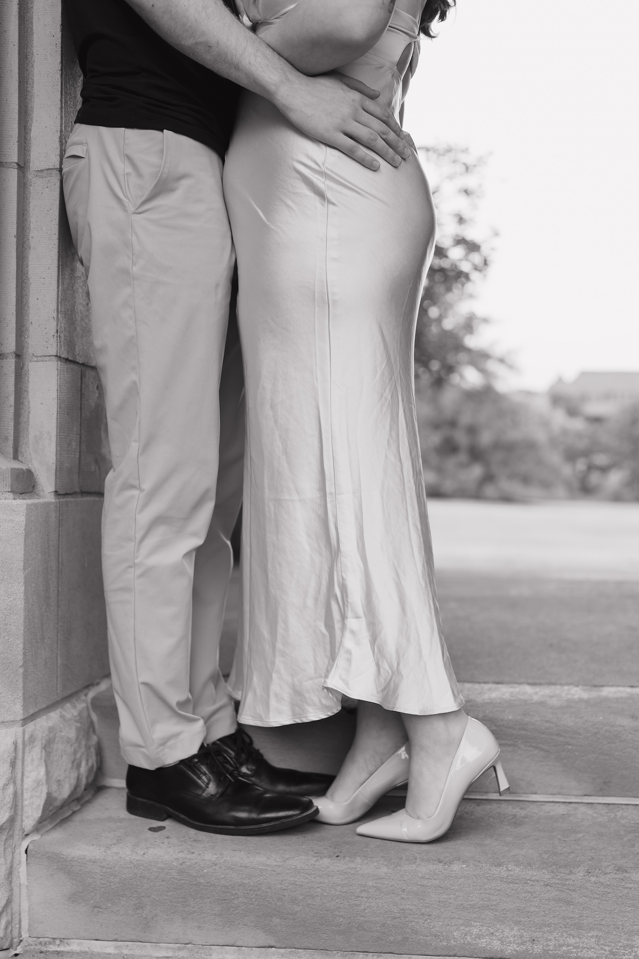 A couple standing close together outside a classic stone building, smiling softly as they lean their foreheads together during an engagement session.