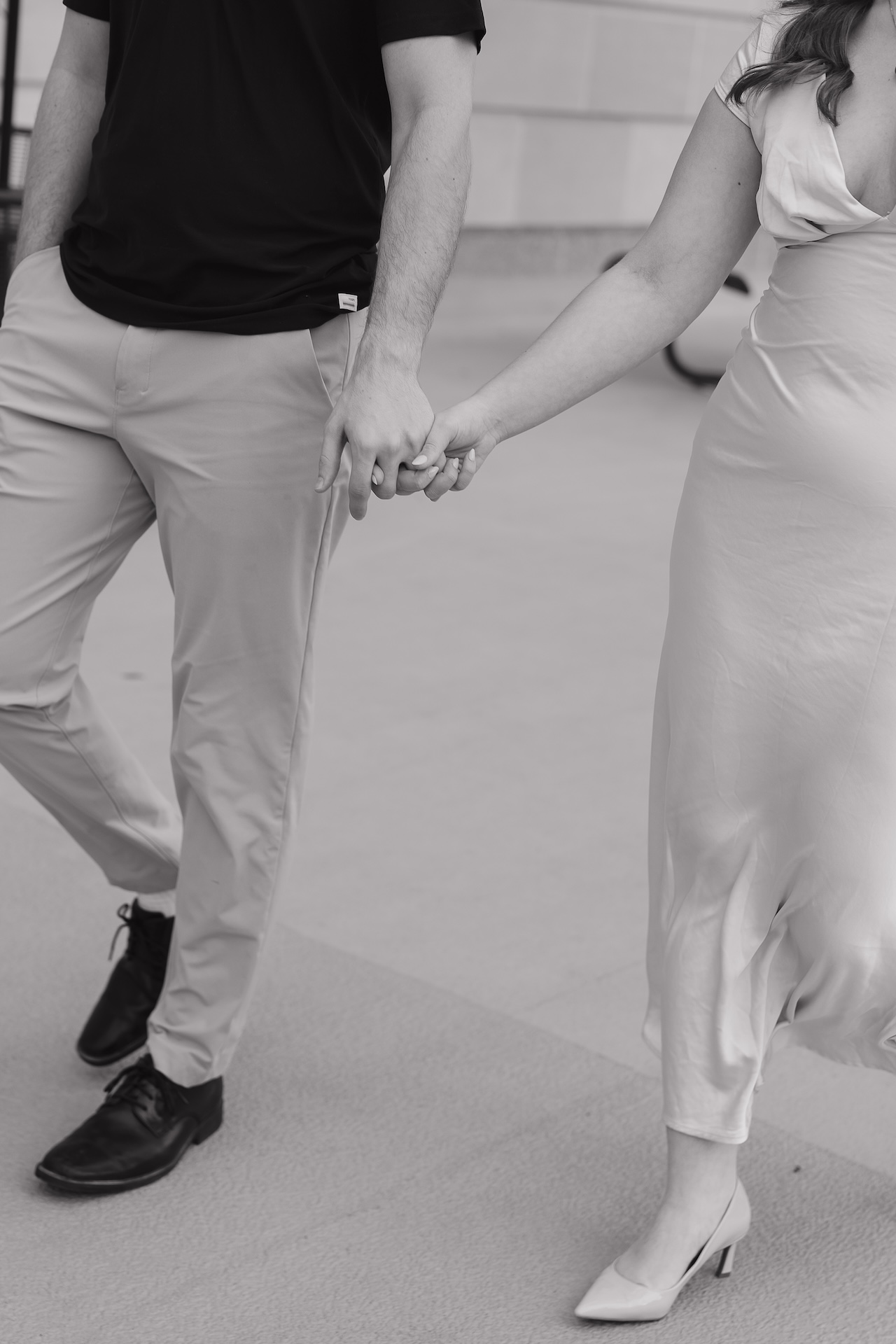 Black and white detail shot of a couple holding hands while walking, focusing on connection and movement during their engagement session.
