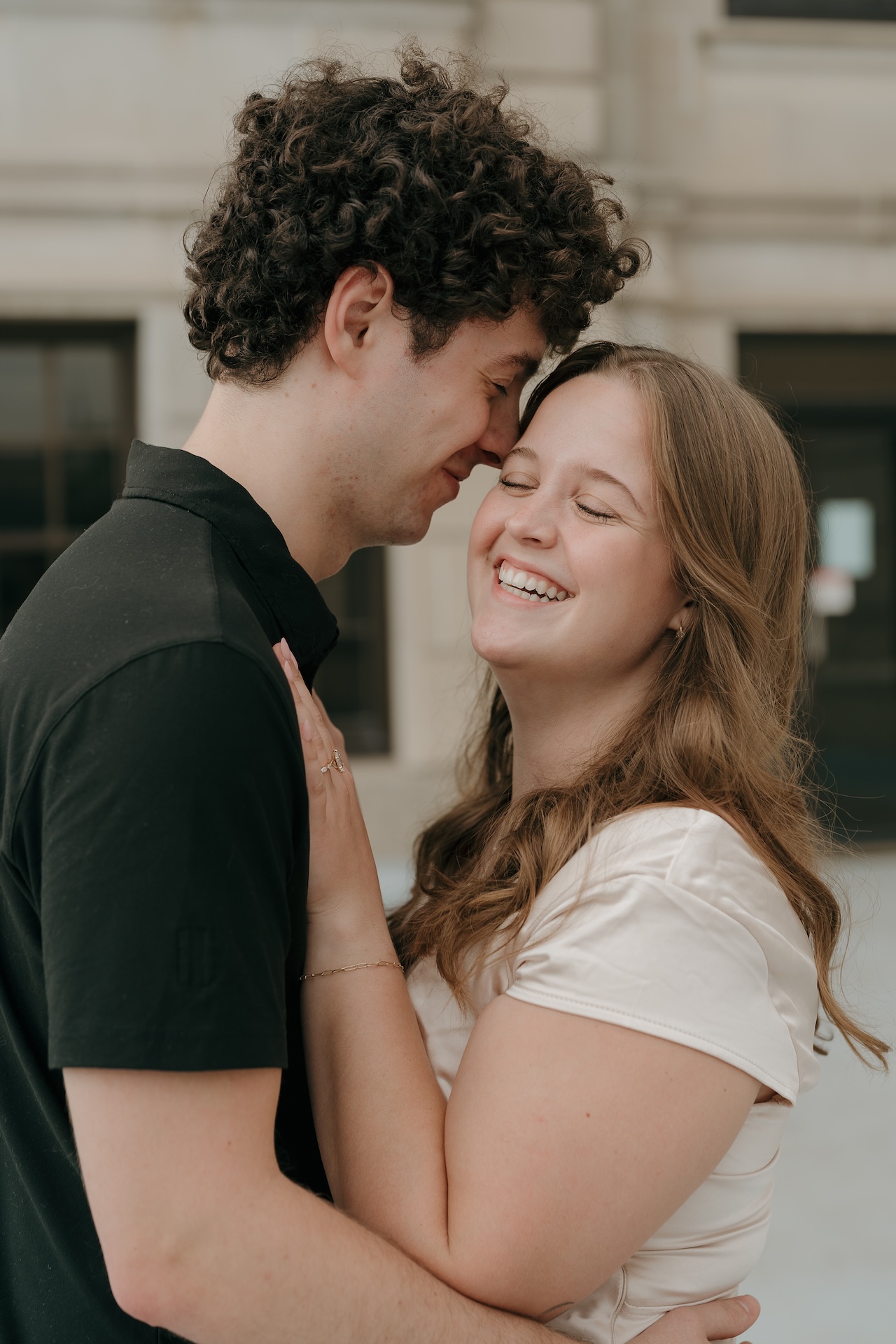 A couple laughing together while embracing outside a historic building, showcasing relaxed and natural engagement portraits.