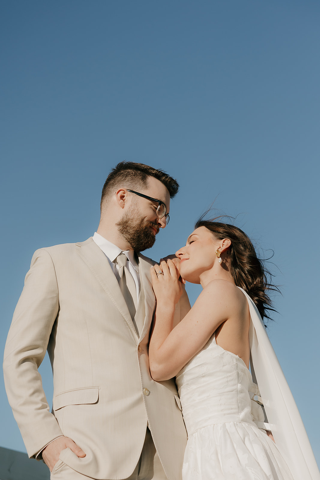 Close-up romantic portrait of a bride and groom embracing during golden hour in a rural field, with the groom kissing the bride’s forehead.