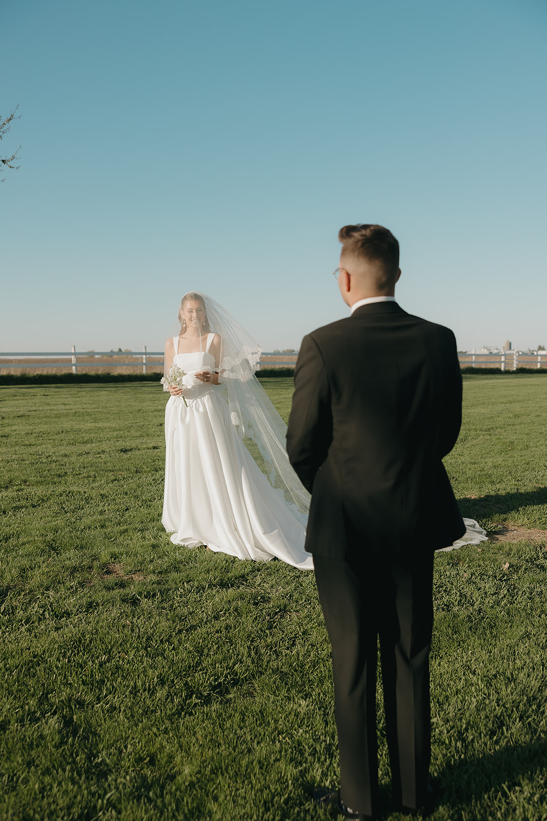 Bride and groom during a first look in an open grassy field under a blue sky, capturing an emotional outdoor wedding moment.