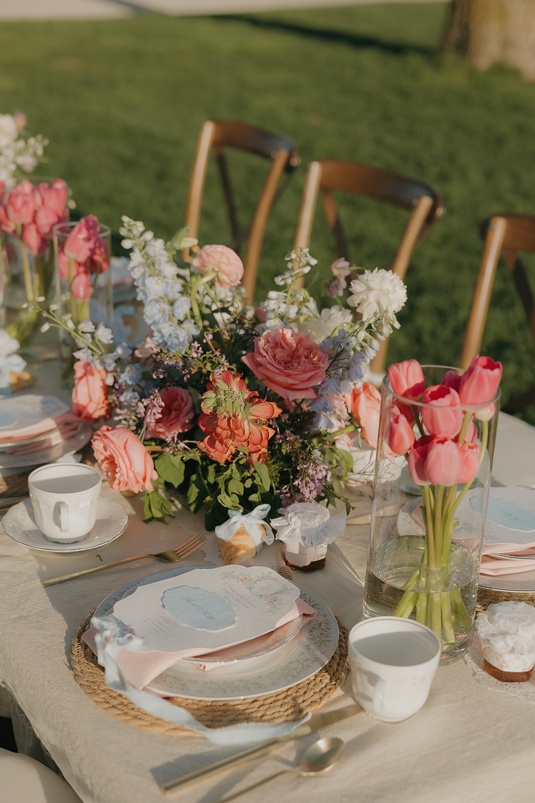 Close-up of pastel wedding tablescape with layered place settings, pink tulips, floral centerpieces, and delicate linens in outdoor spring light, inspired by a wedding vendor checklist for cohesive styling.