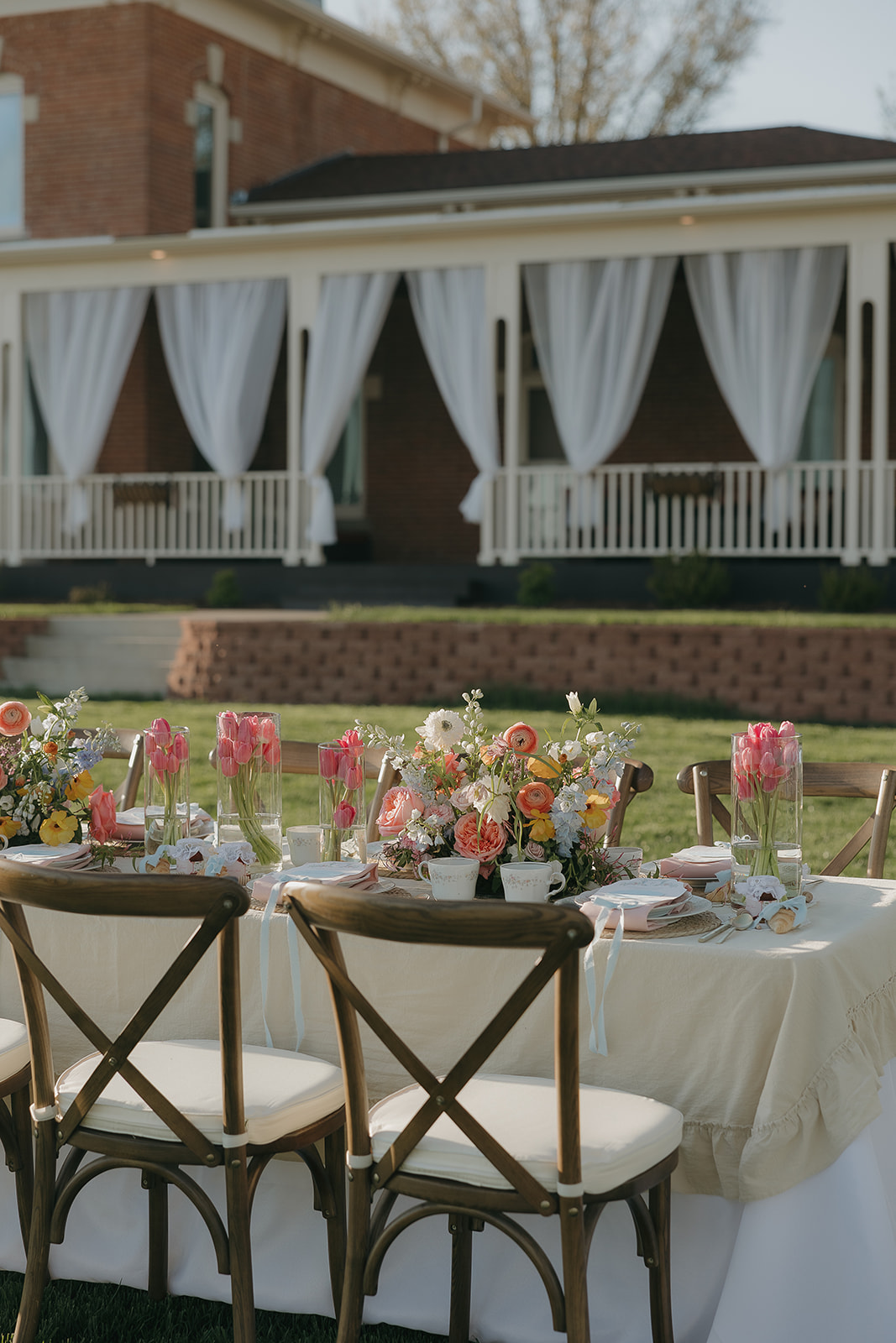 Spring outdoor wedding table with pastel florals, pink tulips, and elegant place settings in front of a historic brick venue, inspired by a wedding vendor checklist for curated reception design.