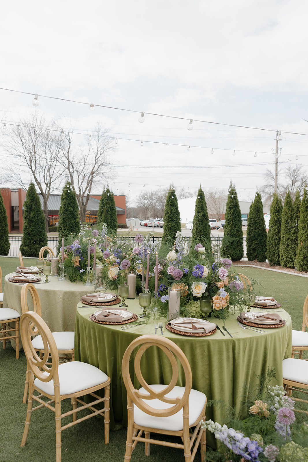 Outdoor spring wedding reception setup with green linens, wooden chairs, pastel florals, and candlelight on a lawn, styled using a wedding vendor checklist for cohesive design.