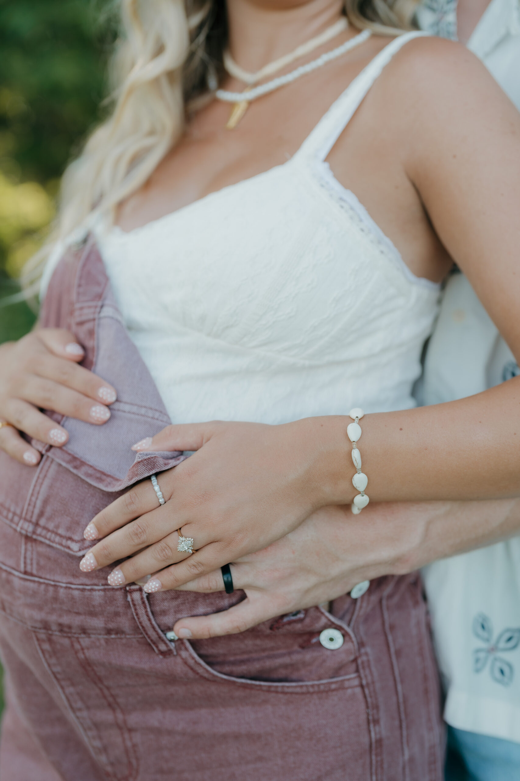 A close-up of the couples hands resting on a baby bump, highlighting rings and jewelry through the quiet storytelling style of documentary wedding photography.