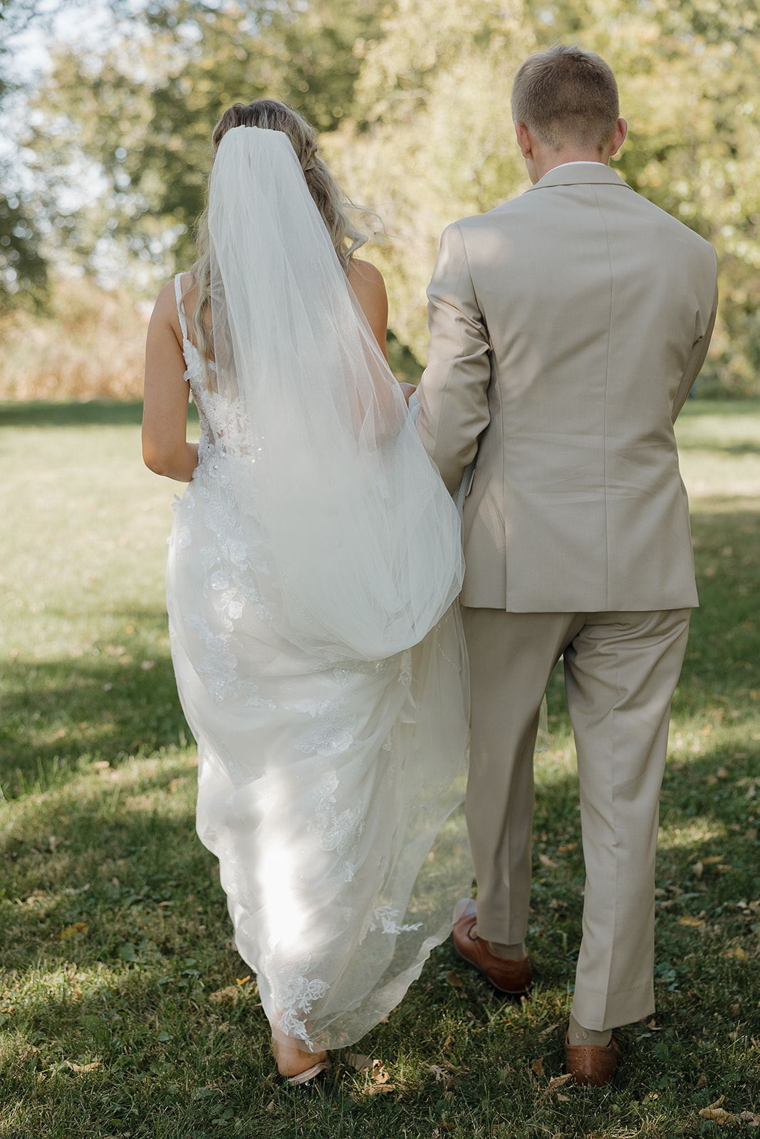 The couple walks away together across a grassy field, their backs turned as documentary wedding photography captures the feeling of the day unfolding naturally.