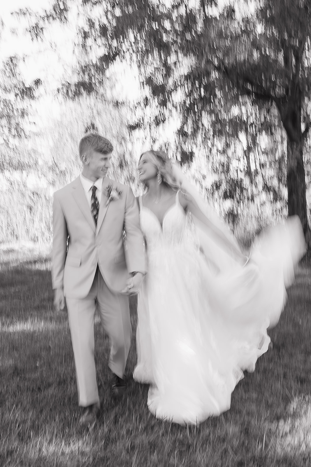 A bride and groom walk hand in hand across an open field, captured in a soft motion blur that reflects the emotion and movement of documentary wedding photography.