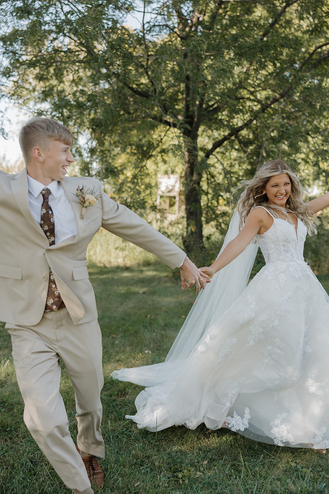 The newlyweds run hand in hand through the grass, laughing freely while their movement is preserved through documentary wedding photography.