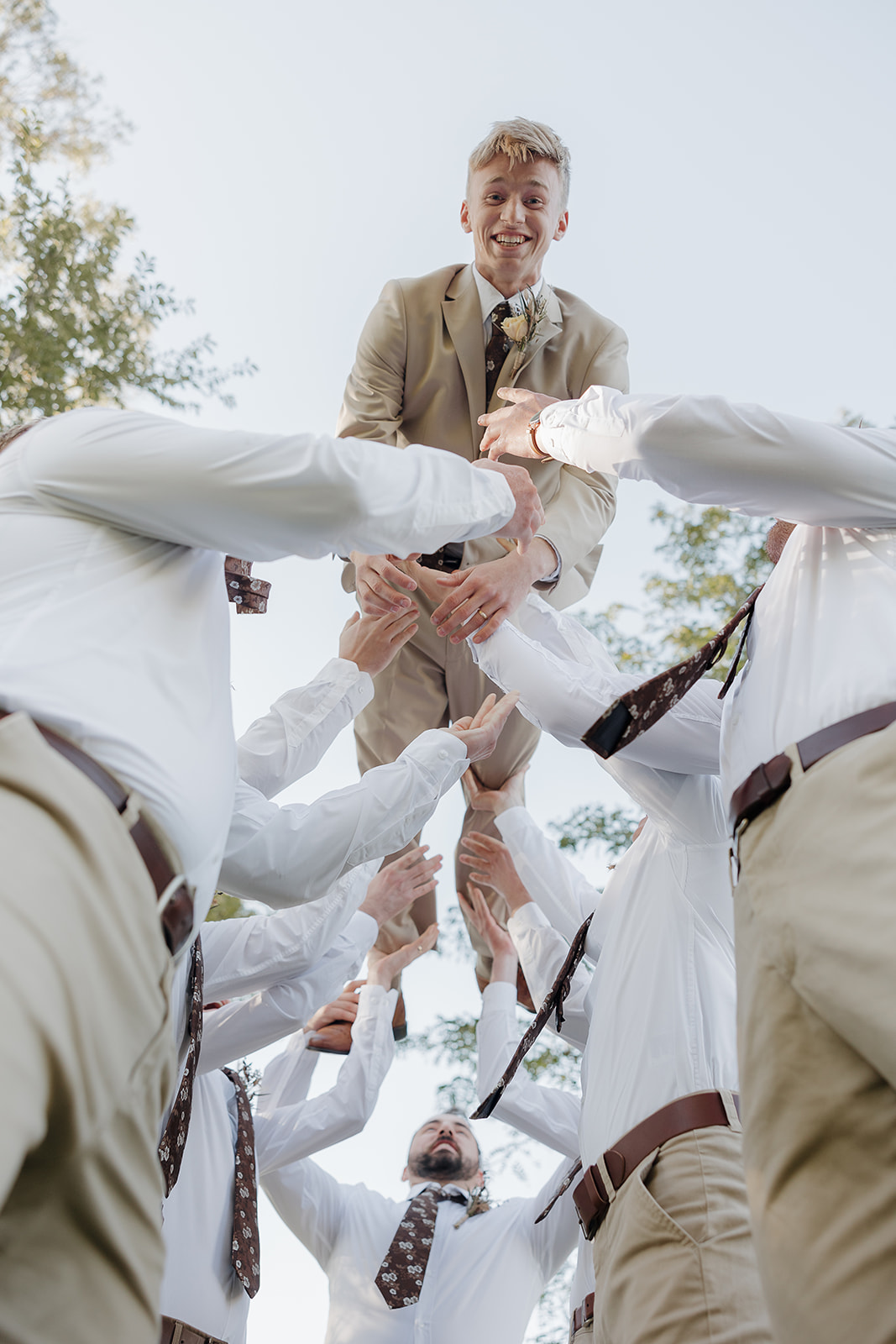 A groom is lifted into the air by his groomsmen during the celebration, photographed from below to preserve the energy and joy of documentary wedding photography.