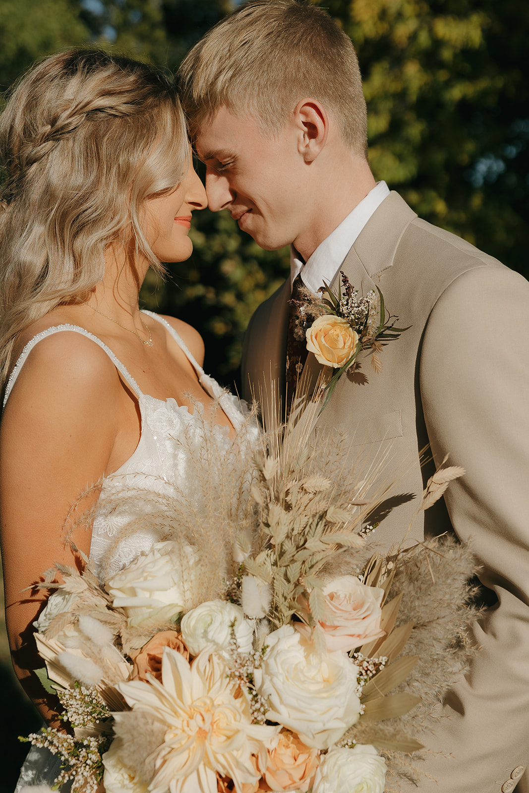 A bride and groom stand close together holding a neutral-toned bouquet, their foreheads touching in a romantic moment captured with documentary wedding photography.
